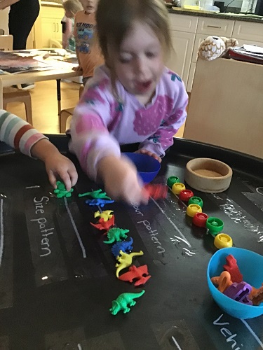 A preschooler is using small coloured dinosaur toys to create a pattern.