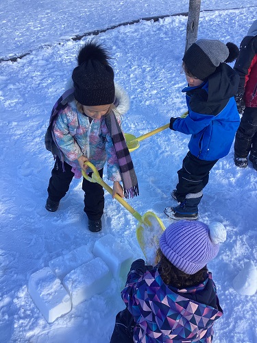 School-age children filling wheelbarrow with snow