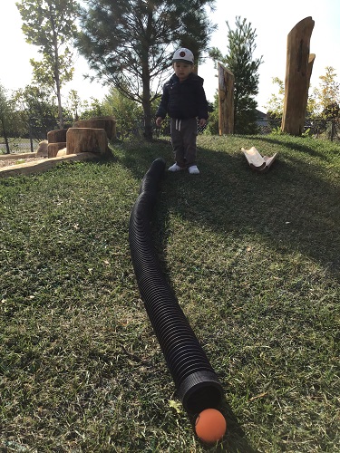 toddler exploring balls and tubes on hill