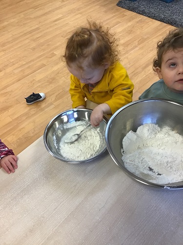 Two toddlers are mixing dry ingredients for the cupcakes.
