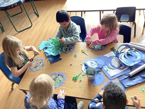 A group of school age children working together at a table making their own world suncatchers