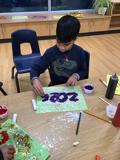 A school age child using paint and glitter to create a 2026 poster