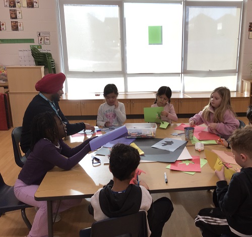 An educator sitting with a group of children at a table doing art