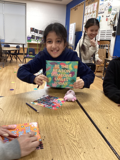 A school age child holding up a poster that says "be the reason someone smiles today"