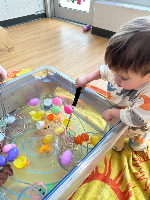 A child using a scoop with water and plastic eggs.
