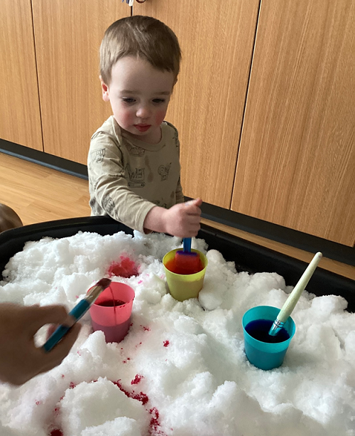 A child picking up a paint brush to paint the snow