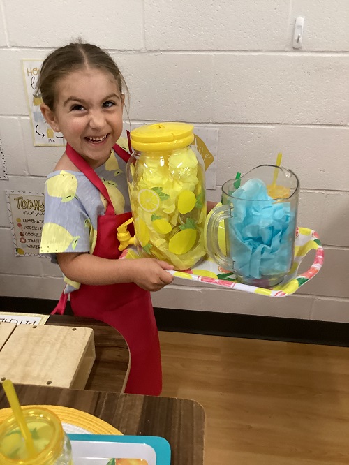 A child engaged with pretend play as they hold a tray of lemonade.