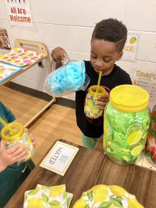 A child engaging in pretend play as they enjoy a cup of lemonade.