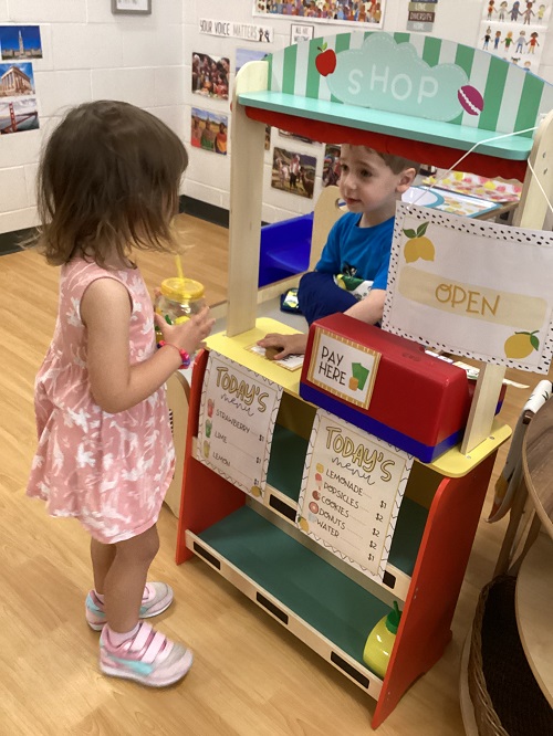 A child purchasing a cup of lemonade from the dramatic-play lemonade stand.