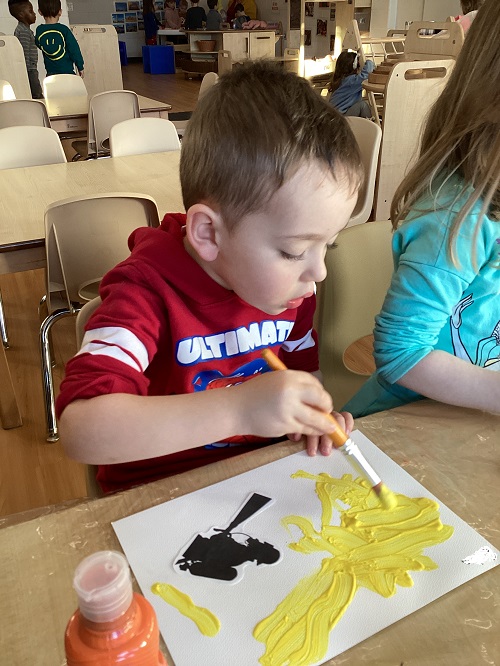 A child sitting at a table painting incorporating their firefighter silhouette.