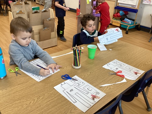 Two children at a table working on paper robots