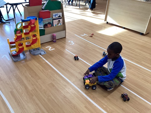 A child sitting with monster trucks on the track.