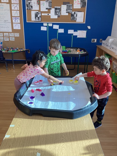 A small group of children using cars to paint with.
