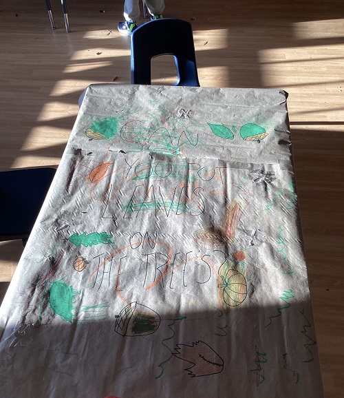 Kraft paper covering a table with an invitation for children to put leaves on the tree