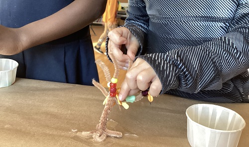 School age children using fine motor skills to place beads on a pipe cleaner tree