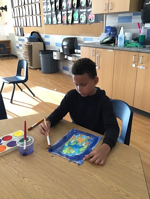 A school age child using water colours to paint a Norval Morrisseau inspired piece of art 