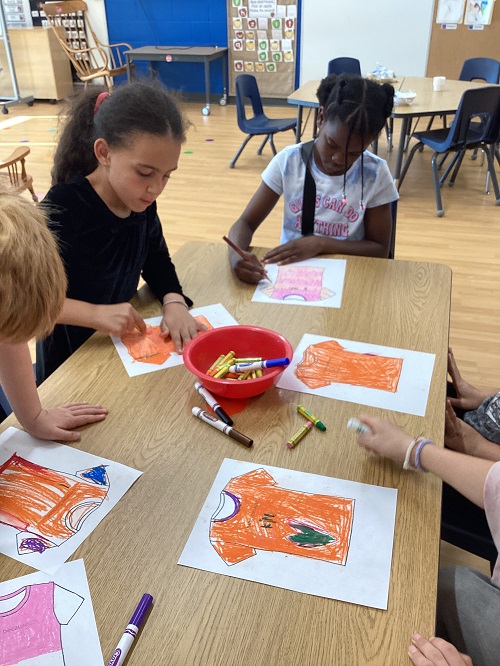 School age children working at a table colouring orange shirts