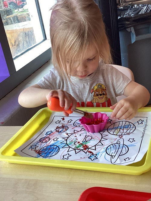 A child applying glitter to their picture.