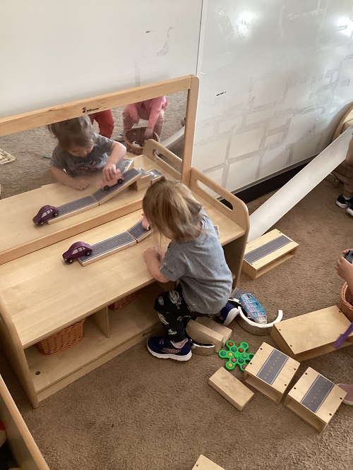A child driving their car along the track they created using blocks.