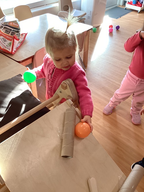A toddler placing a ball at the top of the ball ramp