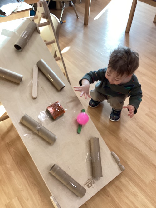 A toddler watching a ball go down the ball ramp