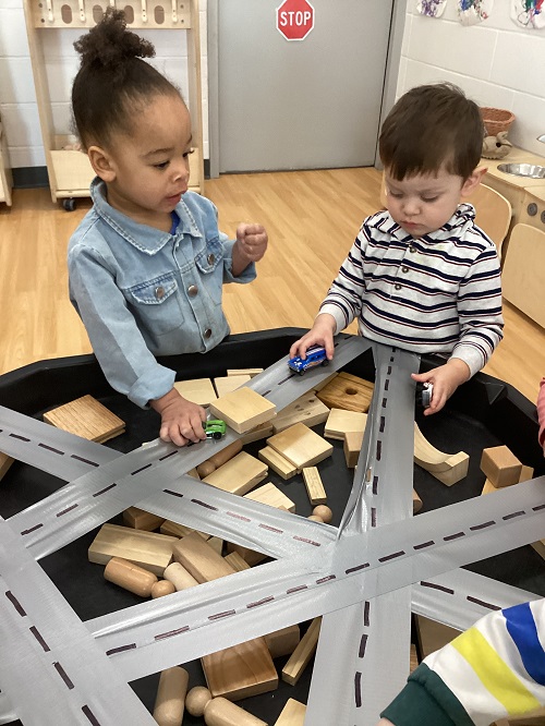 Two children engaging with the track and vehicles in the tuff tray