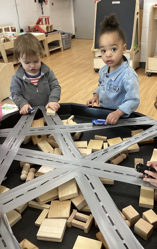 Two children exploring with vehicles and a track