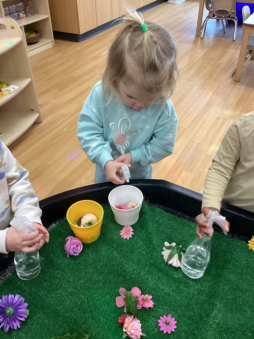 A toddler child using a spray bottle to water artificial flowers