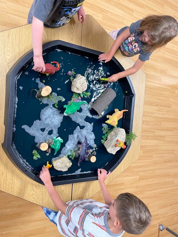 A small group of children engage in exploration with a dino-themed tuff tray.