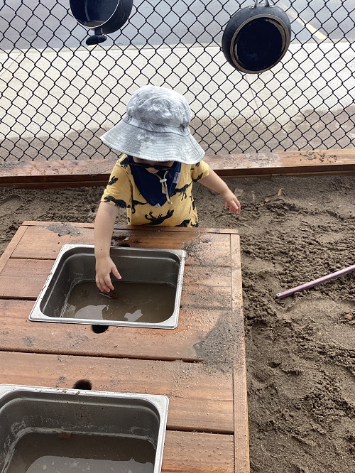 A child getting ready to dip their hand in the sink water in the mud kitchen.