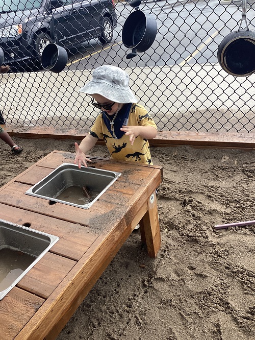 A child exploring the sink water in the mud kitchen.