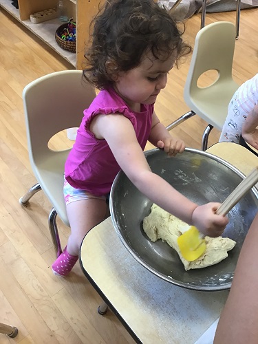 Child sitting at the table with a metal bowl with a spatula stirring the dough in the bowl