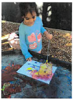Toddler child standing at the tuff tray with a fly swatter with paint on paper in front of her