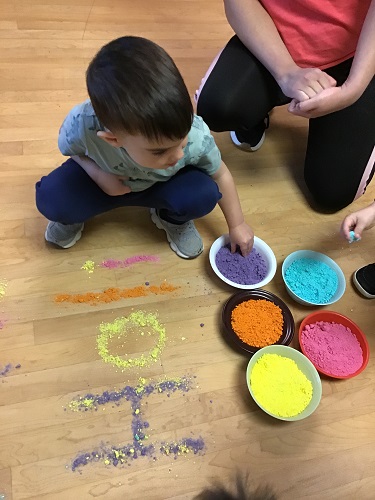 A child looking at bowls of colourful powder for Holi celebration