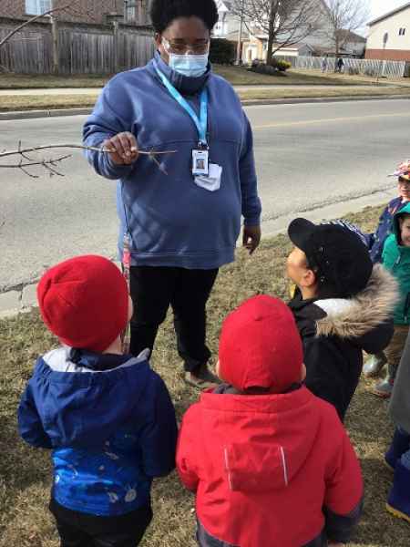 educator holding a tree branch, talking to children