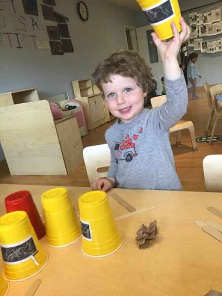 boy picking up a cup to reveal a piece of paper under it