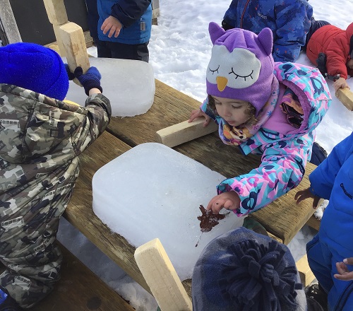 children exploring a large chunk of ice and snow