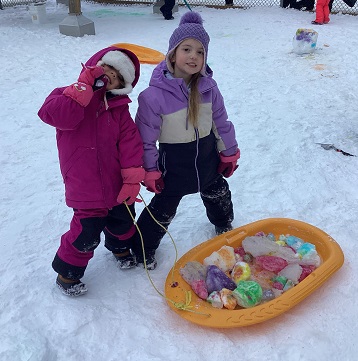 Children standing behind a sled full of colourful ice chunks