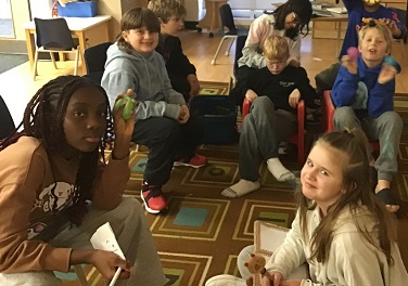group of children sitting on the carpet and on chairs posing for a photo