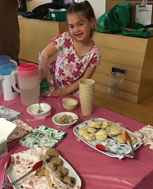 child sitting at a table full of cookies, treats and tea
