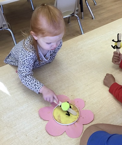 child exploring a bee activity with a pink flower