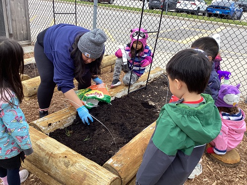 children watching and helping an educator work in the garden bed