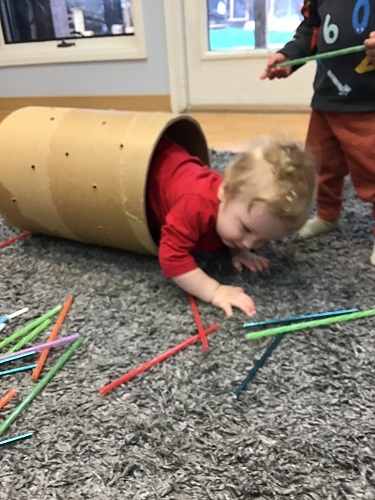 An infant is crawling through a large cardboard tube like a tunnel.