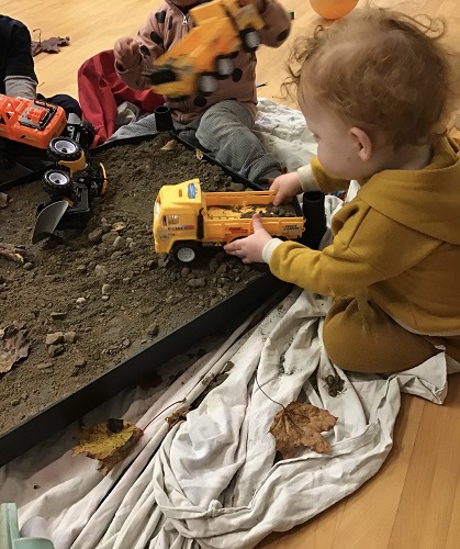 A toddler is driving a construction vehicles in the mud.