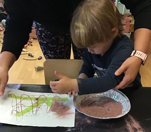 Child being helped by educator to sprinkle sand