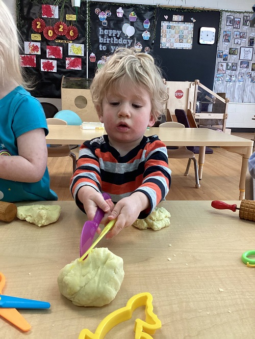 Child cutting their playdough with a material