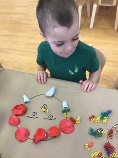 Child creating a face on paper with nature items. 
