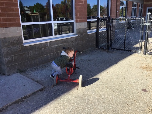 Child trying to climb on a tricycle. 