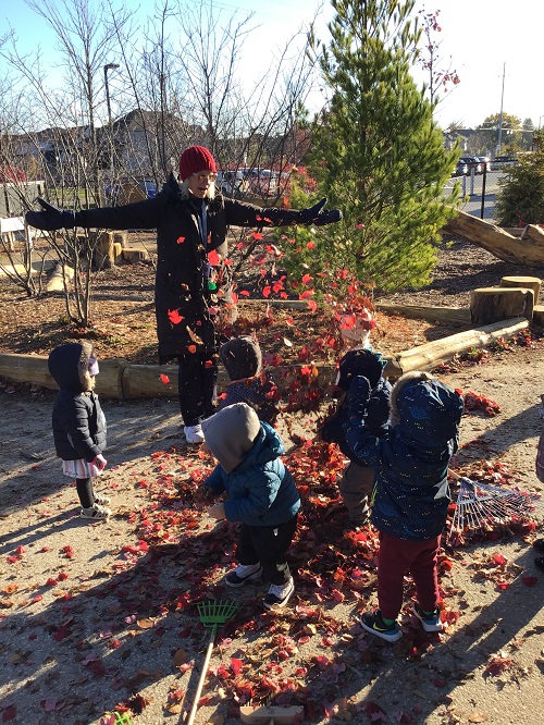 Educator and children throwing leaves up in the air.