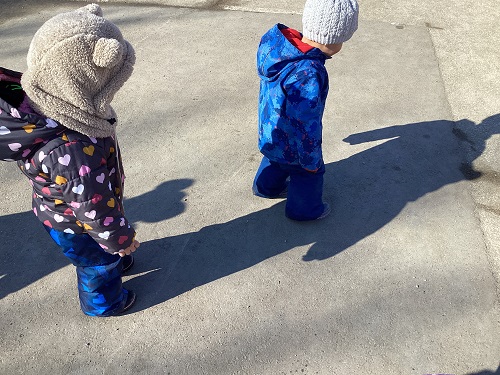 Children discovering their shadows on the pavement.